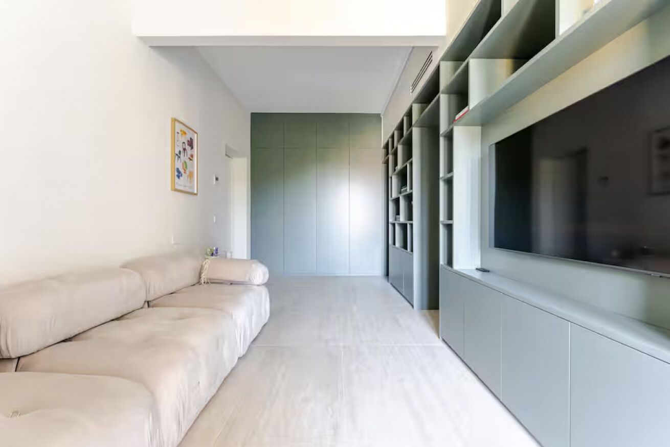 Una sala de estar moderna con un sofá, un televisor y una estantería de pared.