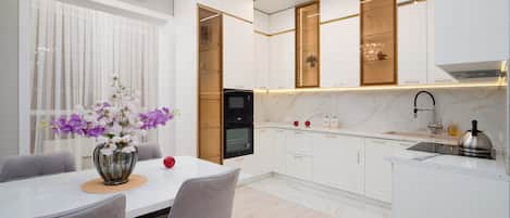 A modern kitchen with white cabinetry, a marble countertop, and a built-in oven.