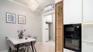 A modern kitchen with white cabinetry, a black oven, and a glass-fronted cabinet. - Spacious 3-room apartments (Almaty)