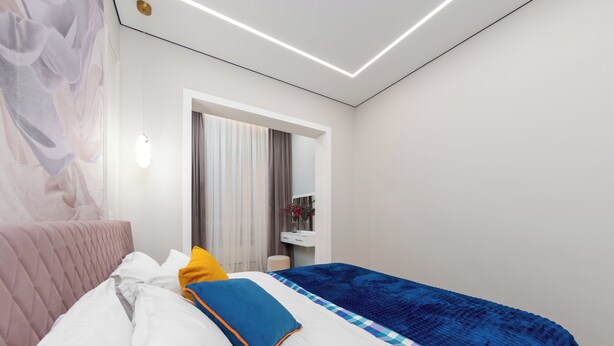 A modern bedroom with a bed, a bedside table, a mirror, and a window with curtains. - Spacious 3-room apartments (Almaty)