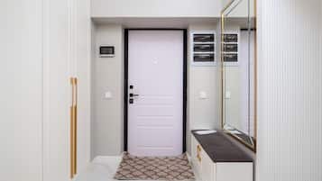 Un couloir avec une porte blanche, un petit tapis, un miroir et une fenêtre à cadre blanc.