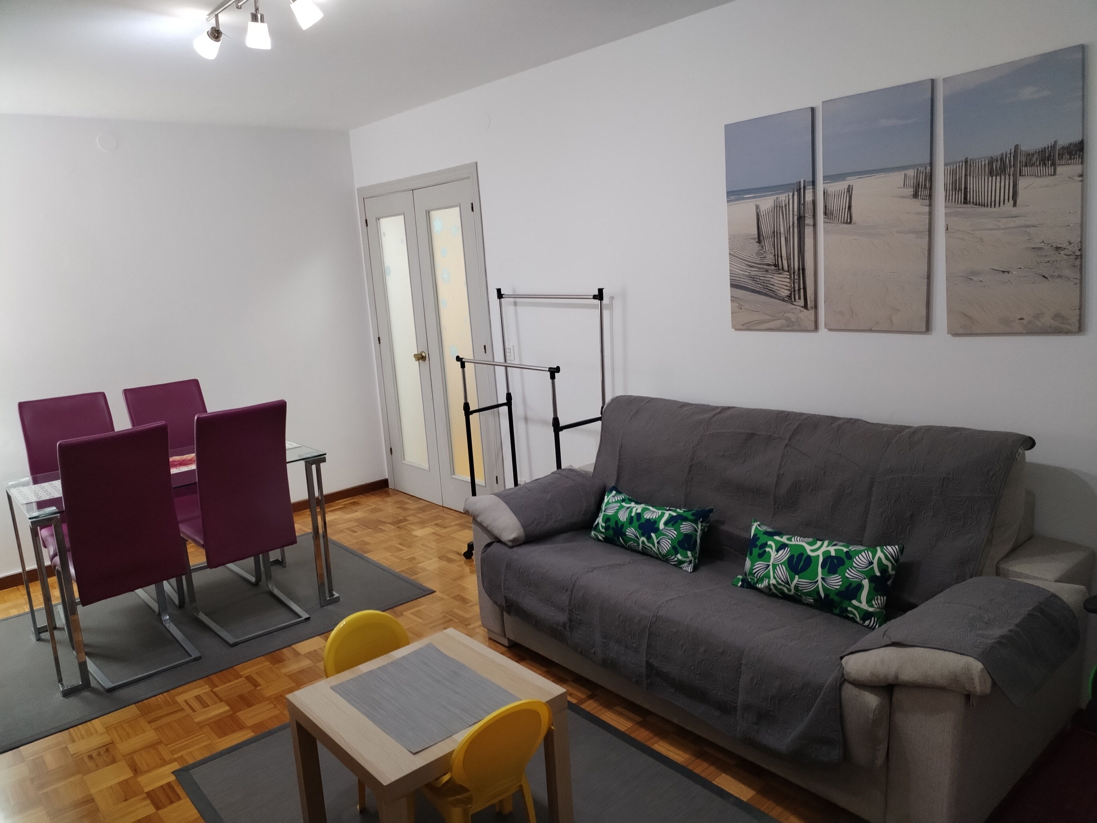 A living room with a grey sofa, purple chairs, a small table, and artwork on the wall.