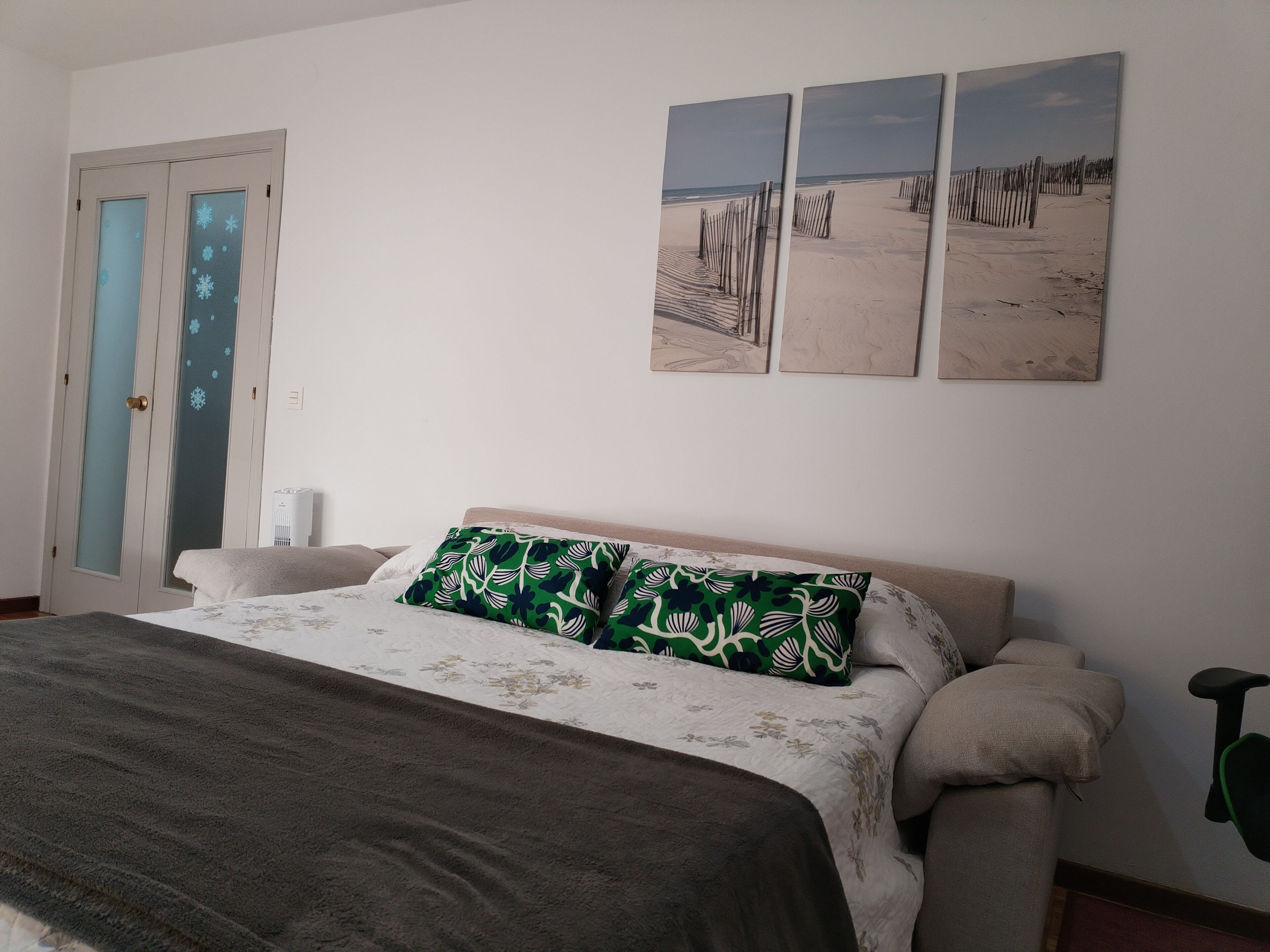 Une chambre à coucher comprenant un lit, une table de chevet, un climatiseur fixé au mur et une porte dotée de panneaux en verre dépoli.