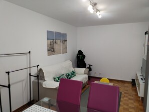 Ein Zimmer mit einem weißen Sofa, einem Gaming-Sessel, einem Glastisch und Holzboden.