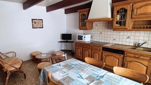 Une cuisine compacte avec des meubles en bois, un pare-feu en carreaux, une table à manger avec des chaises et un petit téléviseur.