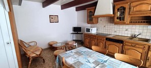 A compact kitchen with wooden cabinets, a tiled backsplash, a dining table with chairs, and a small television.