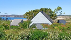 Une maison avec un toit triangulaire, entourée d’une végétation luxuriante et offrant une vue sur l’océan.