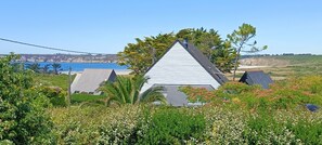 A house with a triangular roof, surrounded by lush greenery and a view of the ocean.