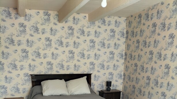 Une chambre à coucher avec un lit, une table de chevet, une commode et un papier peint à motifs.