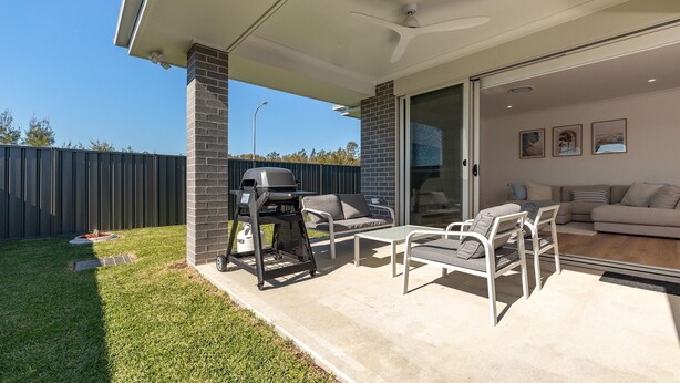 A patio area with a barbecue grill, outdoor seating, and a sliding glass door leading to an interior living space. - Neptune Coastal Retreat (Forster)