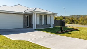 A residential house with a garage, a front porch, and a well-maintained lawn. - Neptune Coastal Retreat (Forster)