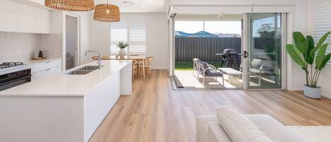 A modern kitchen with a central island, a dining area with a table and chairs, and a patio with outdoor seating.