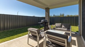 An outdoor patio with a grill, two cushioned chairs, and a table.