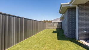 A fenced backyard with a well-maintained lawn, a metal fence, and a brick building. - Neptune Coastal Retreat (Forster)