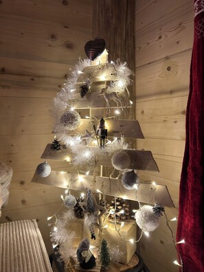 A Christmas tree with lights and ornaments, set against a wooden wall background. - Chalet with Balconies (sleeps 10) (Saint-Michel-de-Maurienne)