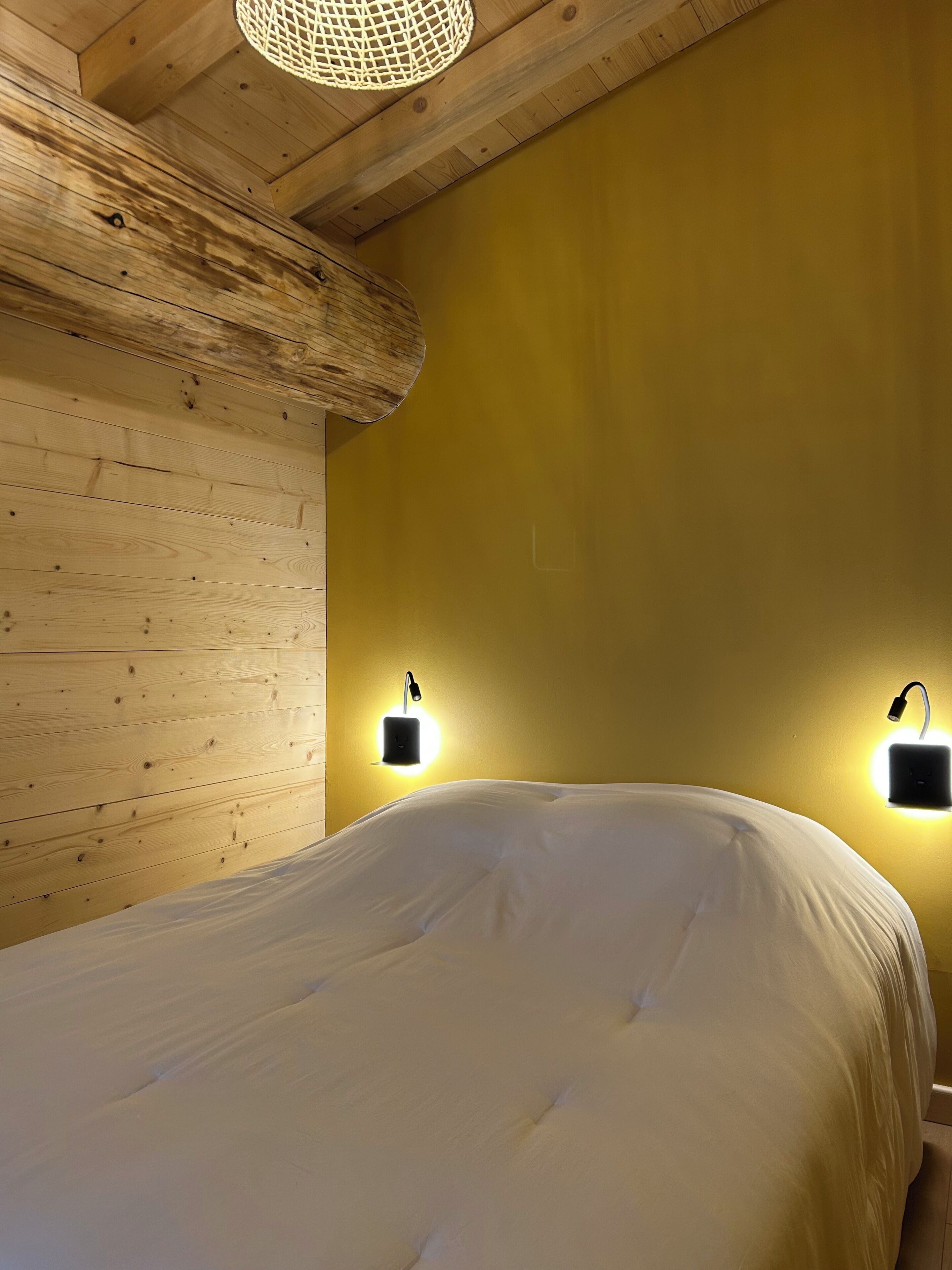 Una camera con soffitto in legno, un letto con biancheria bianca e due lampade a parete.
