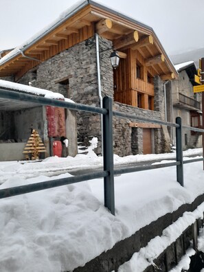 A stone building with a wooden upper structure, a metal railing in front, and snow on the ground. - Chalet with Balconies (sleeps 10) (Saint-Michel-de-Maurienne)