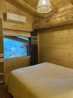 A room with a bed, an air conditioning unit, a window with a view of a stone wall, and a hanging light fixture. - Chalet with Balconies (sleeps 10) (Saint-Michel-de-Maurienne)