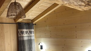 Makuuhuone, jossa on puinen katto, valkoinen peitto sängyllä, riippuvalaisin ja seinään kiinnitetty valaisin.