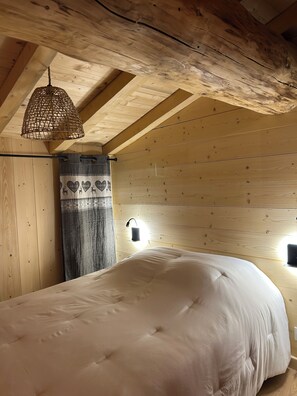 A bedroom with a wooden ceiling, a bed with a white duvet, a hanging light fixture, and a wall-mounted light. - Chalet with Balconies (sleeps 10) (Saint-Michel-de-Maurienne)