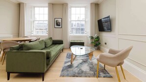 A modern living room with a green sofa, a glass coffee table, and a beige armchair. - Stylish Apartment on Castle Street (Edinburgh)