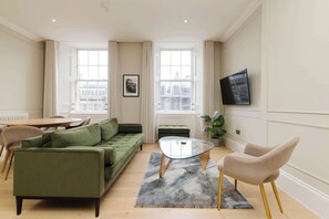 A modern living room with a green sofa, a glass coffee table, and a beige armchair. - Stylish Apartment on Castle Street (Edinburgh)