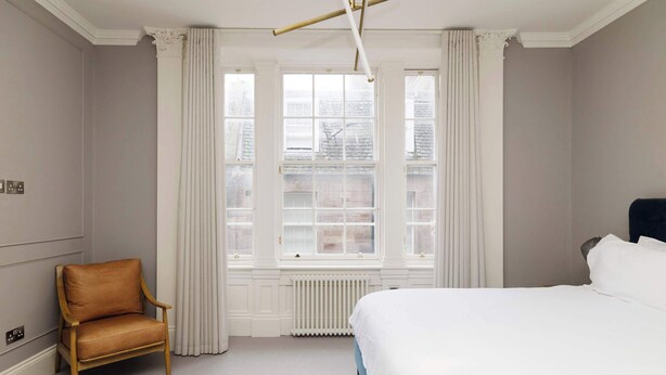 A hotel room with a bed, a chair, a radiator, and large windows. - Stylish Apartment on Castle Street (Edinburgh)