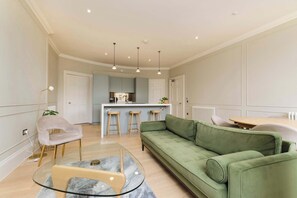 A modern living room with a green sofa, a glass coffee table, and a bar area in the background. - Stylish Apartment on Castle Street (Edinburgh)