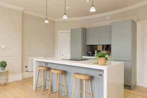 A modern kitchen with a central island, bar stools, pendant lighting, and a built-in oven. - Stylish Apartment on Castle Street (Edinburgh)