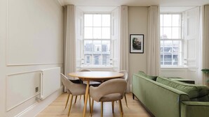 A room with a round table, four chairs, a green sofa, and two windows with curtains. - Stylish Apartment on Castle Street (Edinburgh)
