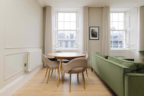 A room with a round table, four chairs, a green sofa, and two windows with curtains. - Stylish Apartment on Castle Street (Edinburgh)