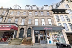 A row of multi-story buildings with various storefronts, including a coffee shop and a spa. - Stylish Apartment on Castle Street (Edinburgh)