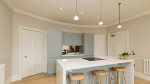 A modern kitchen with a central island, bar stools, pendant lighting, and a view of the adjacent living area. - Stylish Apartment on Castle Street (Edinburgh)