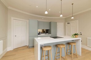 A modern kitchen with a central island, bar stools, pendant lighting, and a view of the adjacent living area. - Stylish Apartment on Castle Street (Edinburgh)