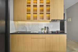 A modern kitchen with wooden cabinets, a black countertop, and a built-in oven. - Brisal by Kozystay - Sudirman (Central Jakarta)