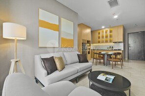 A modern living room with a sofa, a coffee table, and a lamp. There is a kitchen area with wooden cabinets and a dining table. - Brisal by Kozystay - Sudirman (Central Jakarta)
