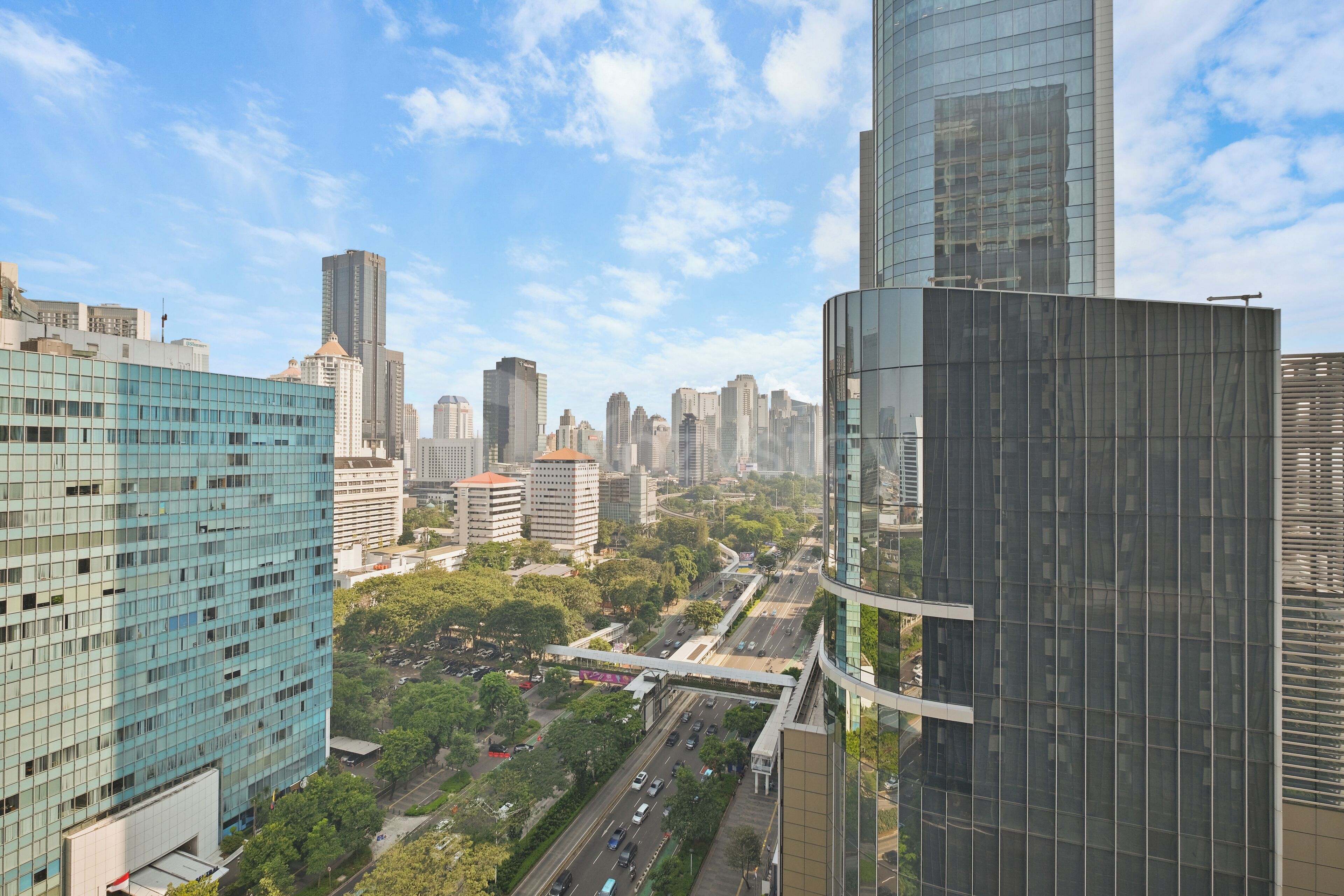 A cityscape with modern high-rise buildings, a clear sky, and a busy road with vehicles.