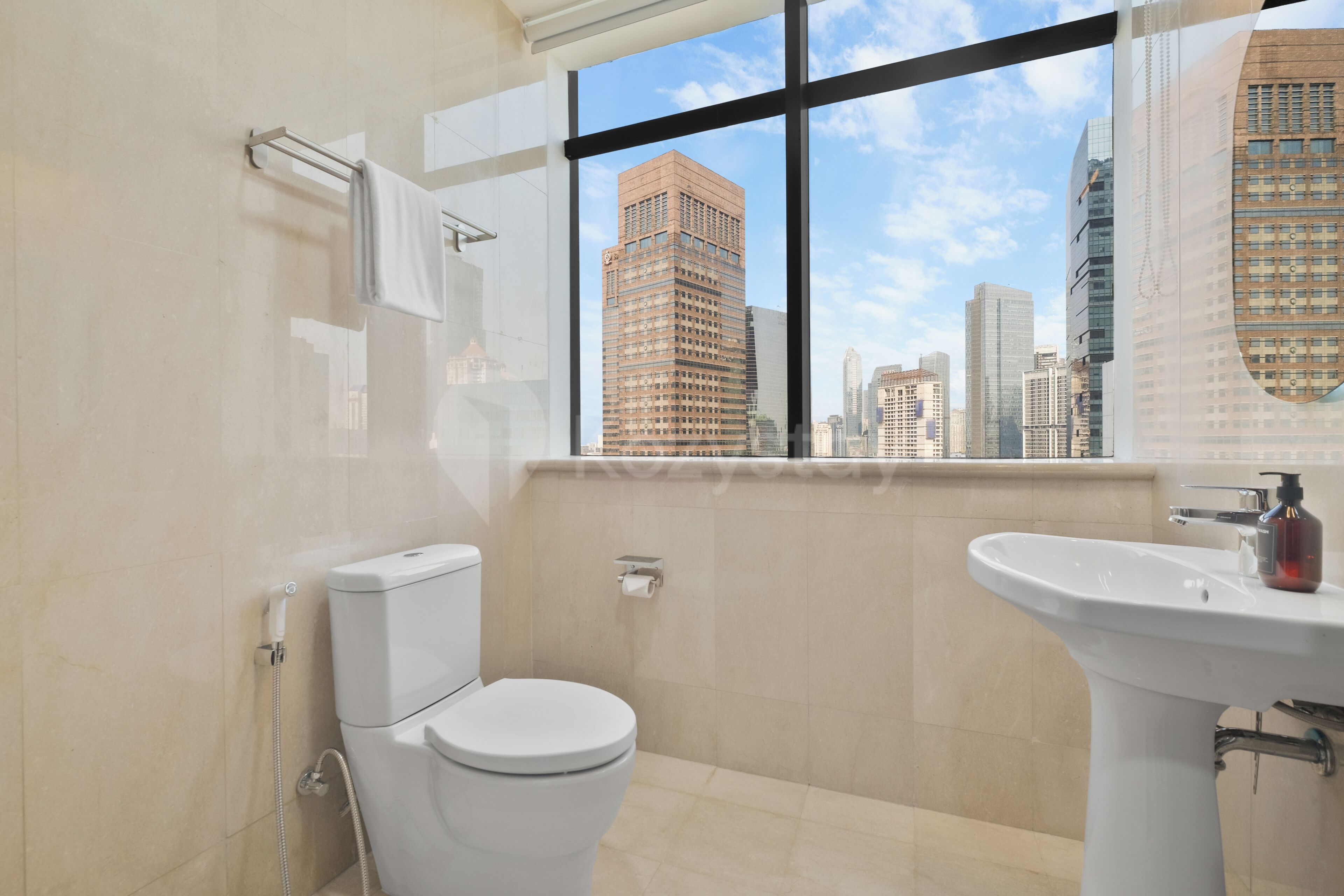 A modern bathroom with a toilet, sink, and a window offering a cityscape view.