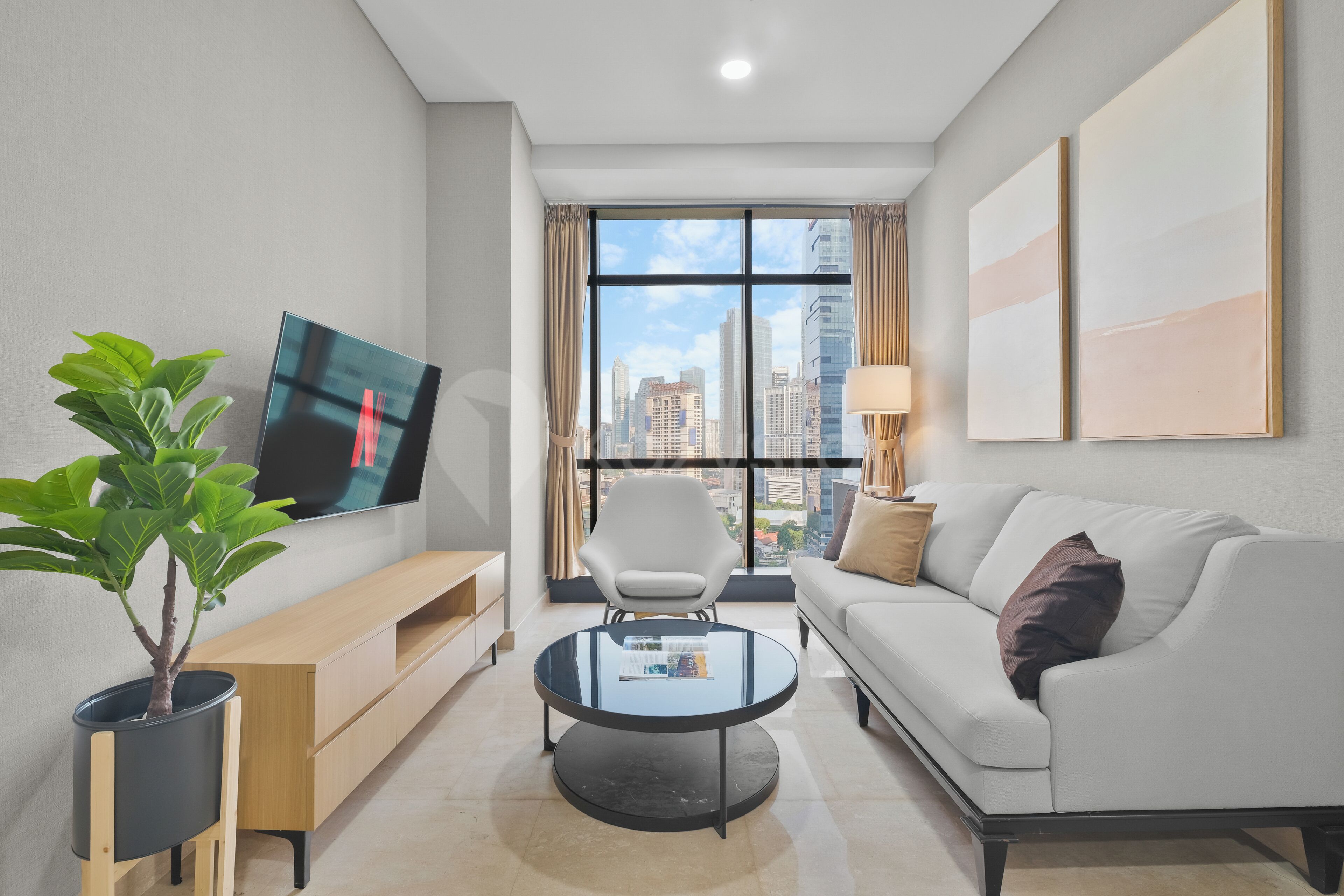 Una sala de estar moderna con una televisión de pantalla plana, una mesa redonda para café, un sofá, una silla y una planta en maceta.