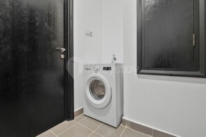 A laundry room with a washing machine, a door, and a wall-mounted light switch. - Brisal by Kozystay - Sudirman (Central Jakarta)