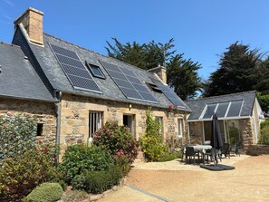 A stone house with a sloped roof, solar panels, and a patio with outdoor furniture. - Le Clos du Verger: 5-Bedroom Family Home (saint quay perros)