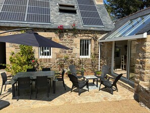 Ein Steinhaus mit Solaranlage auf dem Dach, Außenplätzen und einer überdachten Terrasse.