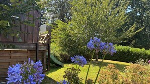 Un giardino con una struttura di gioco in legno, uno scivolo e fiori viola.