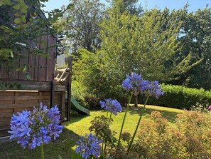 Ein Garten mit einer Spielanlage aus Holz, einer Rutsche und violetten Blumen.