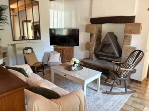 Ein Wohnzimmer mit einer Couch, Sesseln, einem Couchtisch, einem Kamin und einem Fernseher.