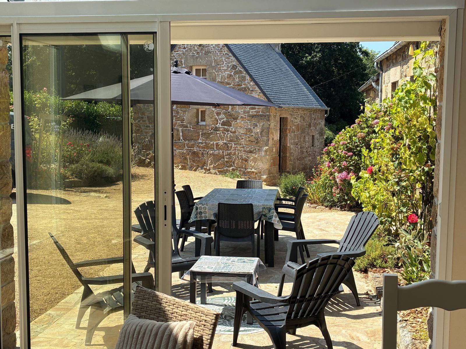 A patio with a table and chairs, a stone building in the background, and a garden with flowers.