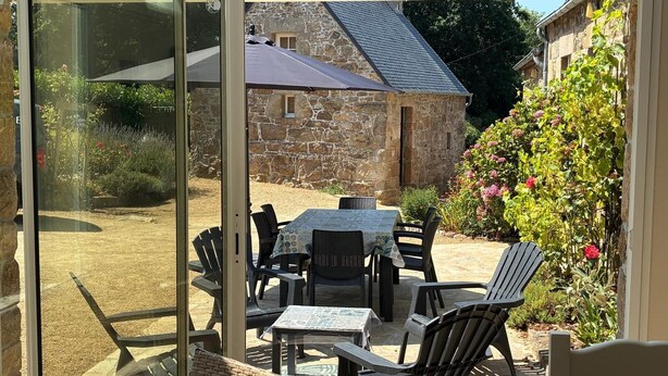 Un patio con tavolo e sedie, un edificio in pietra sullo sfondo e un giardino fiorito.