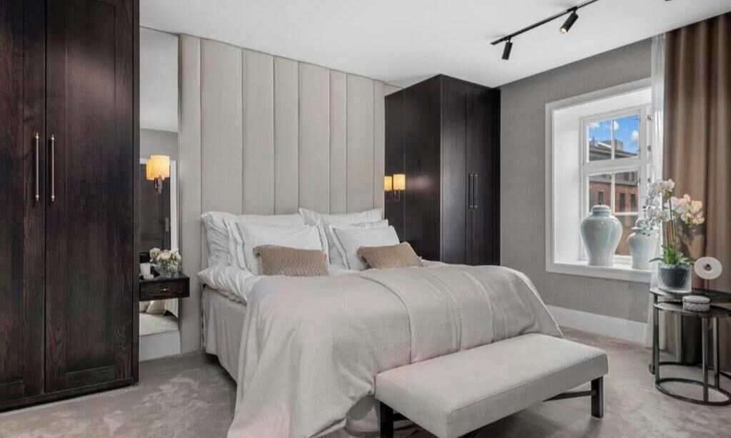 A bedroom with a bed, bedside tables, a bench, a wardrobe, and a window with curtains.