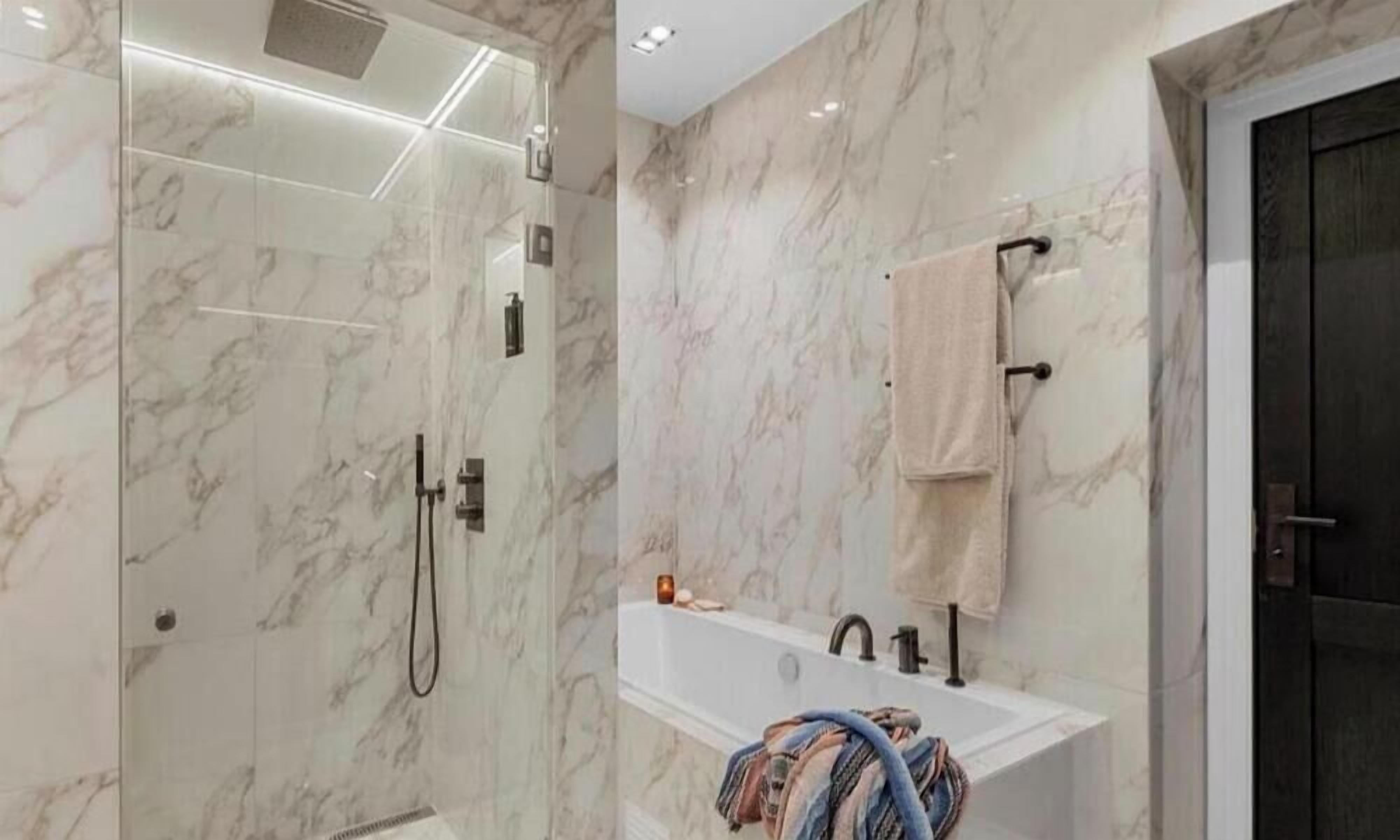 A modern bathroom with a glass-enclosed shower, a freestanding bathtub, and a marble wall.