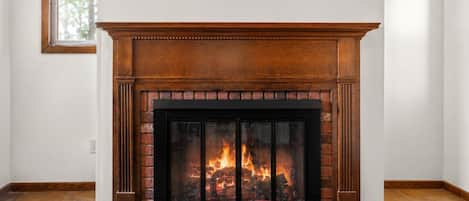 A fireplace with a brick surround and a black glass screen, set in a room with white walls and a tiled floor.